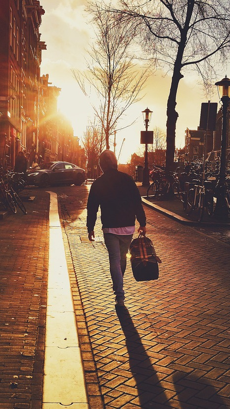Man with a gym bag walking through a street into a sunset
